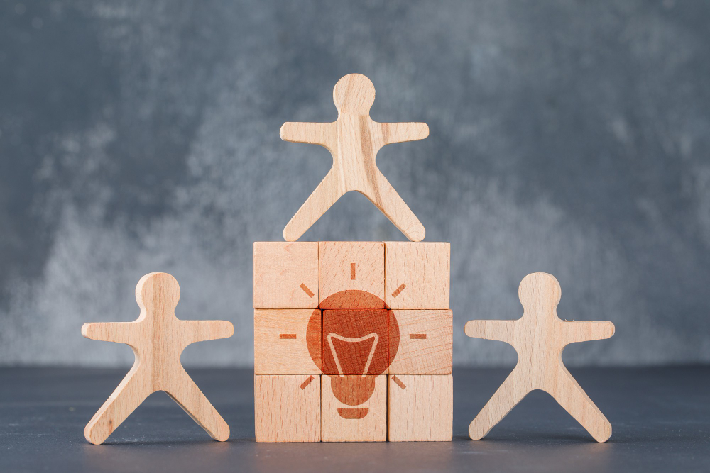 Three human-look figure made with wood while stacking blocks that forms a light bulb icon