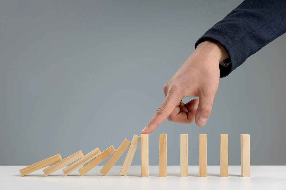 A person's hand stopping the flow of the falling dominos