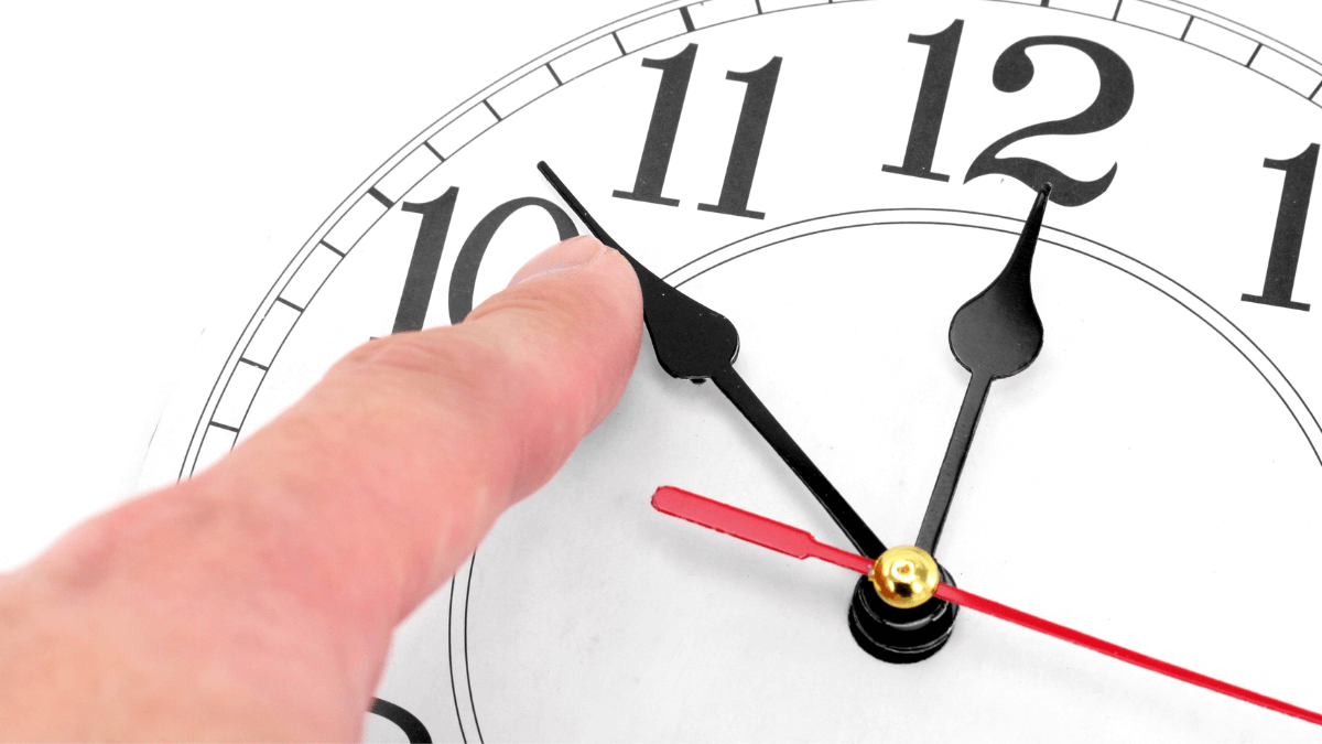 A person's finger trying to change the time through a clock hand