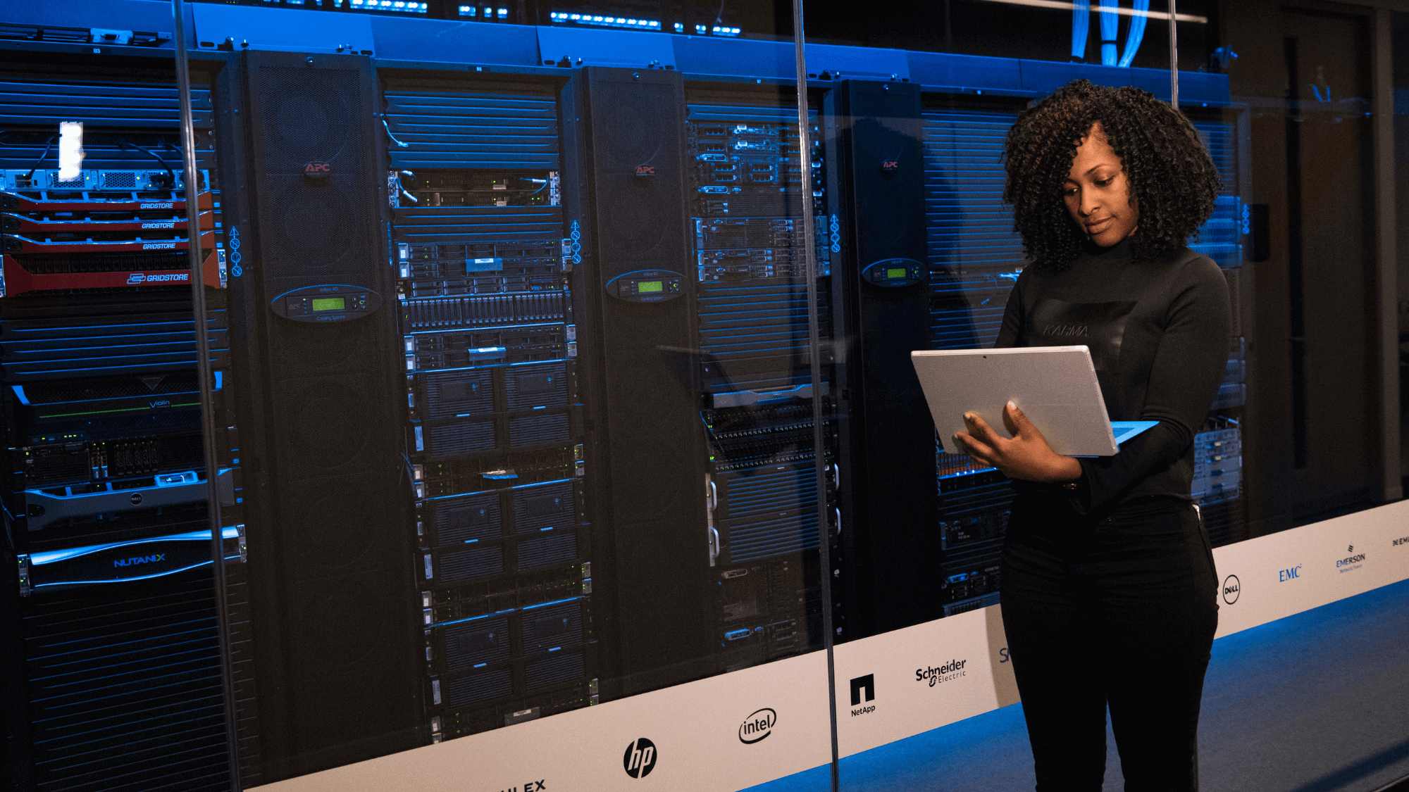 A person standing beside large machines while holding a laptop