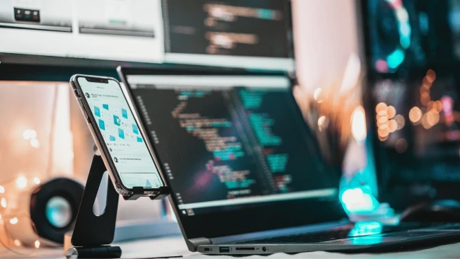 An image of a phone and a laptop displaying HTML codes in the background